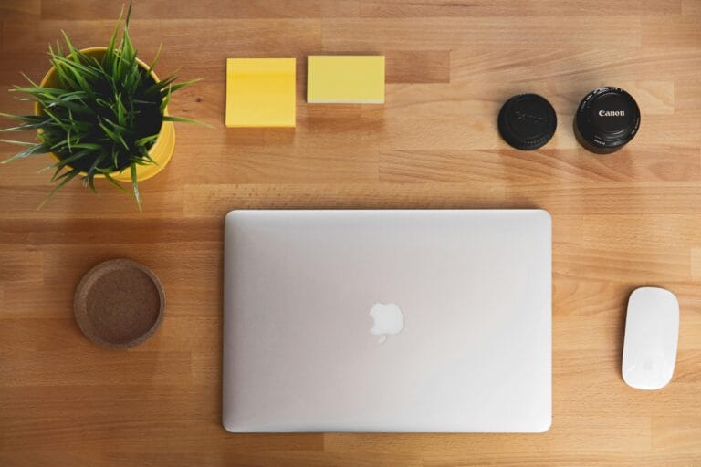 A top-down view of a clean wooden workspace with a laptop, plant, and accessories.